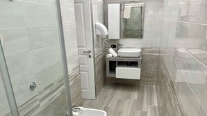 Un baño moderno con cabina de ducha de vidrio, un lavabo blanco y un bidé.