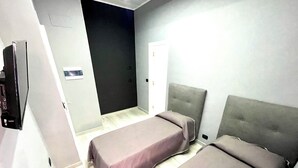 Habitación de hotel con dos camas, un televisor y una puerta que da a otra habitación.