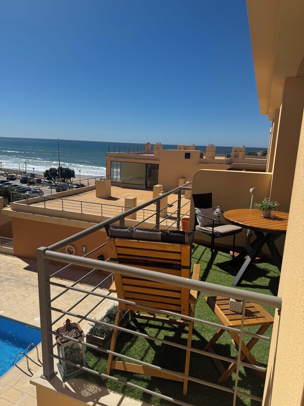 A balcony with a view of the ocean, a pool, and a small table with chairs.