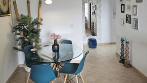 A dining area with a glass table, blue chairs, and a potted plant. - 1 Bedroom Areia Branca Beach (Lourinhã)