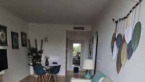 A modern living room with a white sofa, a patterned rug, and a dining area with a table and chairs. - 1 Bedroom Areia Branca Beach (Lourinhã)