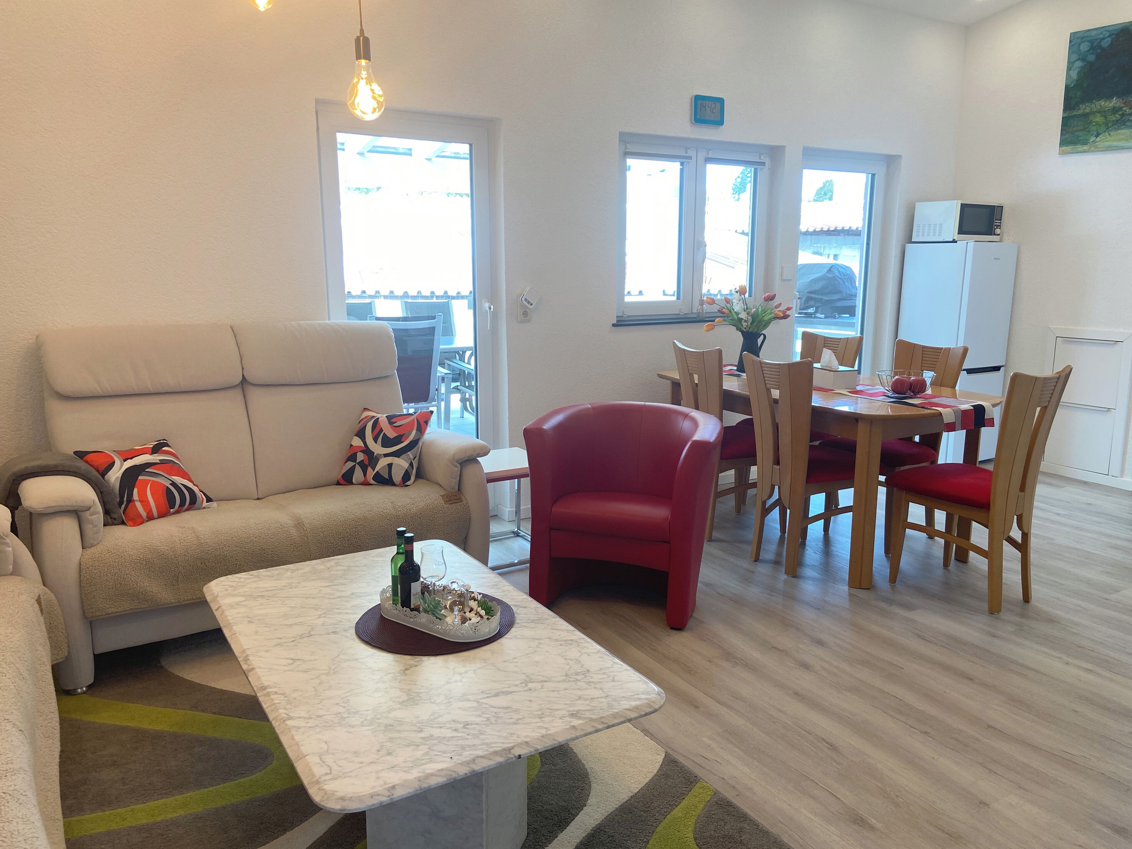 Ein modernes Wohnzimmer mit einem beigefarbenen Sofa, einem roten Sessel, einem Marmor-Couchtisch und einem Essbereich mit Holzkohle und einem Tisch.