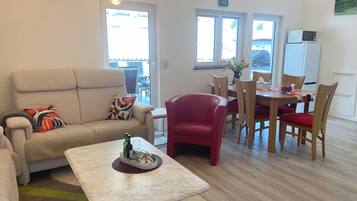 Ein modernes Wohnzimmer mit einem beigefarbenen Sofa, einem roten Sessel, einem Marmor-Couchtisch und einem Essbereich mit Holzkohle und einem Tisch.