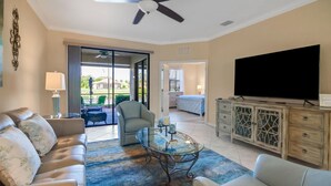 A spacious living room with a glass coffee table, leather sofas, a flat-screen TV, and a view of the outdoors through a sliding glass door.