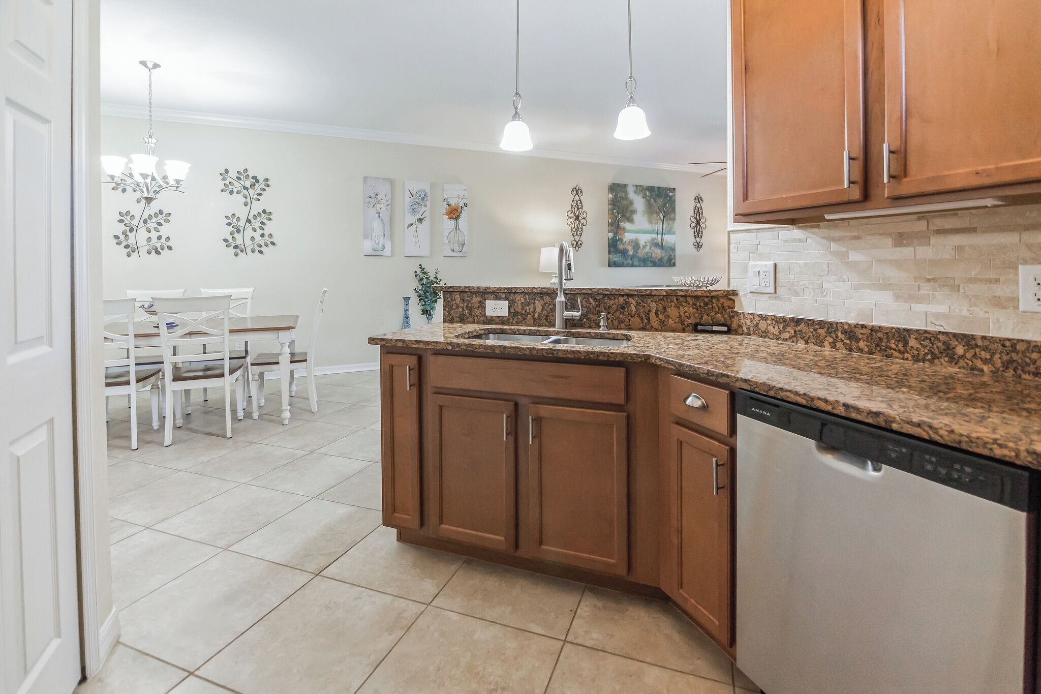A kitchen with granite countertops, wooden cabinets, a dishwasher, and a dining area with a table and chairs.