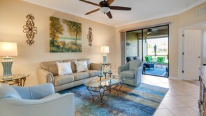 A living room with a beige sofa, a glass coffee table, a blue armchair, and a large painting on the wall.