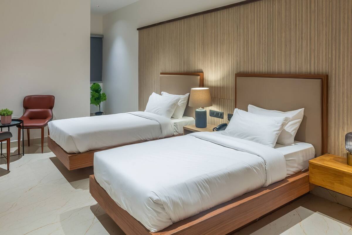 A hotel room with two beds, a desk, a chair, and a small table with a plant.