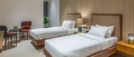 A hotel room with two beds, a desk, a chair, and a small table with a plant.
