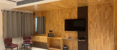 A modern room with a wooden wall panel, a flat-screen TV, a desk, two chairs, and a trash bin.