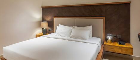 A neatly made bed with white linens, a wooden headboard, and a nightstand with a lamp and a phone.