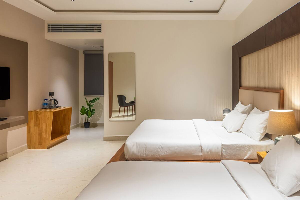 A hotel room with two beds, a TV, a wooden side table, and a mirror.
