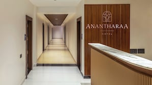 Un'area reception di un hotel con un lungo corridoio che porta alle camere, una scrivania in legno per la reception e un cartello con scritto 'Anantharaa Hotel'.
