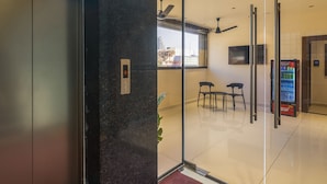 Una hall moderna con una porta in vetro, un'area relax con sedute, un distributore automatico e vista sulla città attraverso la finestra.