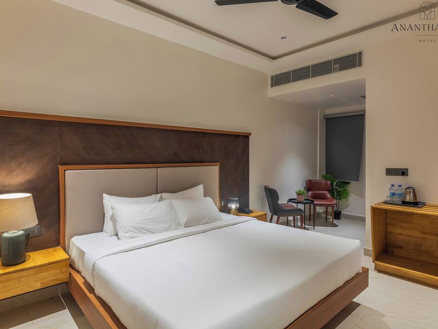 A hotel room with a large bed, a desk, a chair, a lamp, and a ceiling fan.