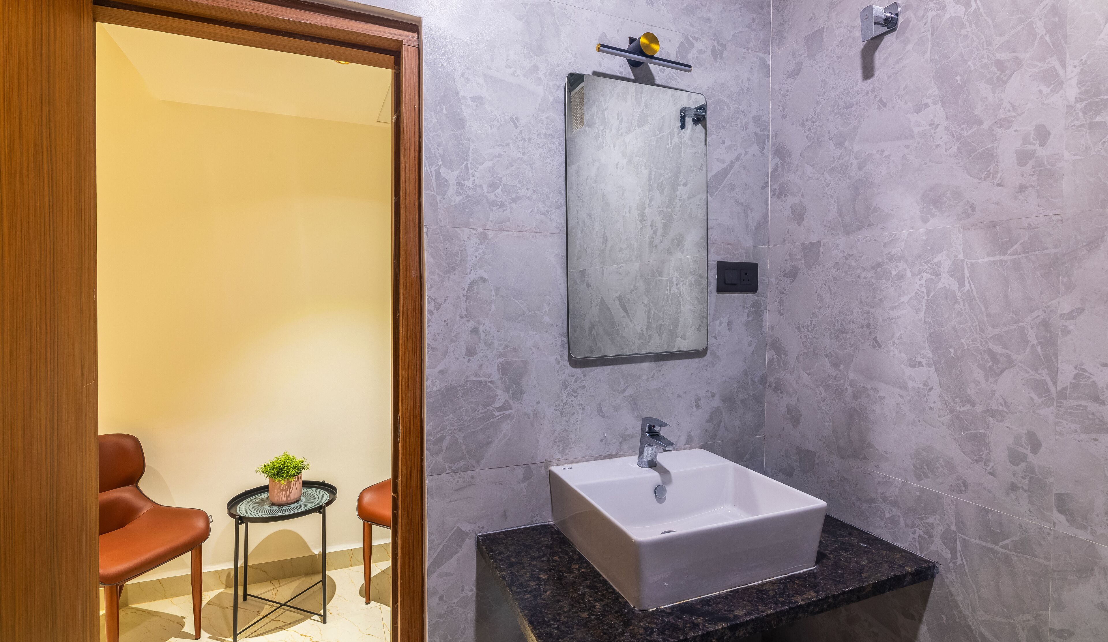 A modern bathroom with a large mirror, a white sink, and a small potted plant.