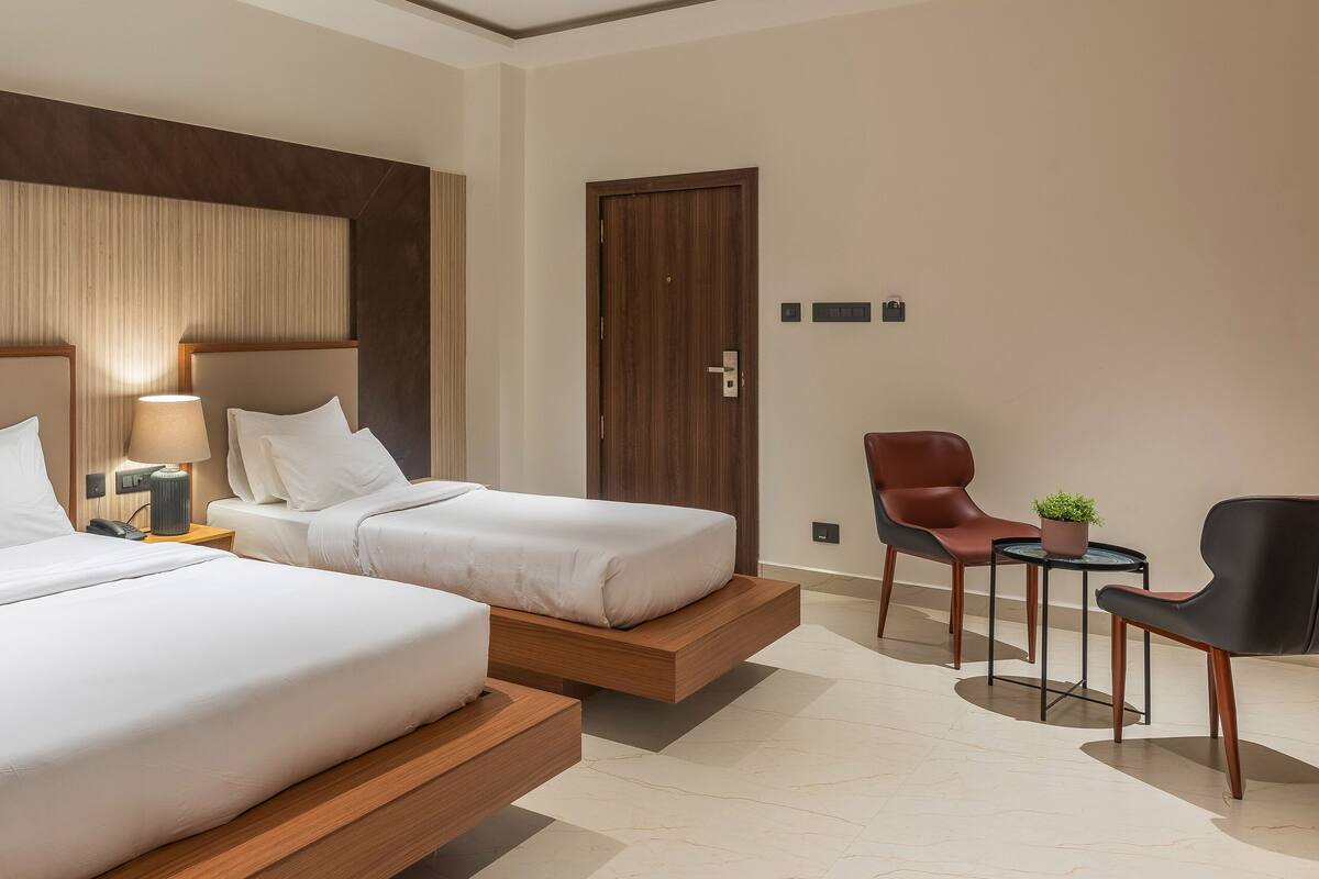 A hotel room with two beds, a desk, a chair, and a door.