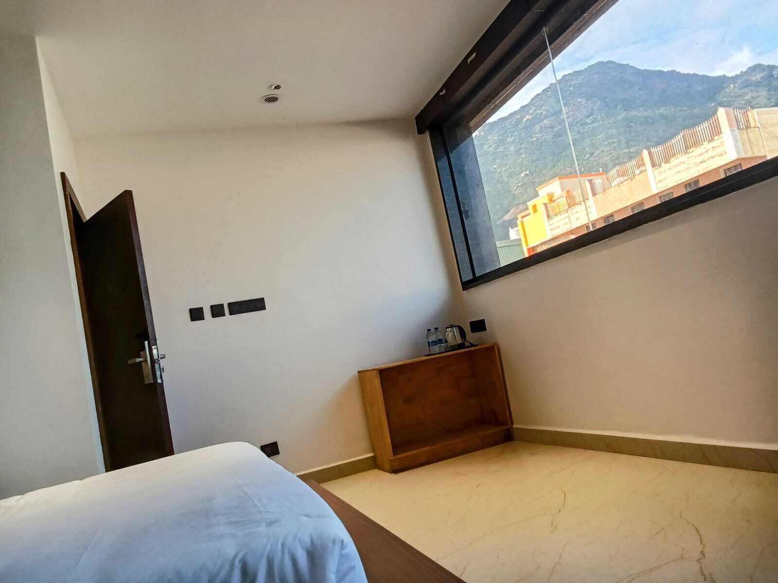 A bedroom with a bed, a small wooden nightstand, a window with a mountain view, and a door.