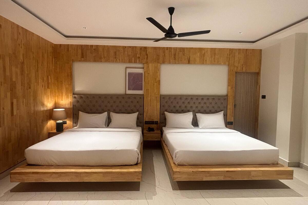A double room with two beds, wooden paneling, a ceiling fan, and a nightstand with a lamp.