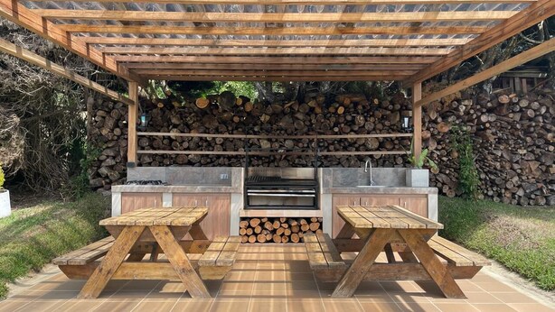 Un área de barbacoa al aire libre con una parrilla, dos mesas de picnic y una estructura de pérgola.