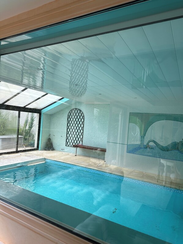 An indoor swimming pool with a clear glass ceiling, a bench, and a decorative wall mural.