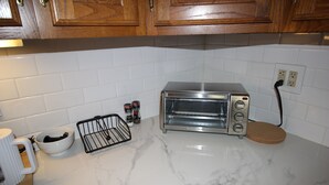 Uma cozinha com bancadas de mármore branco, forno elétrico, cafeteira e armários de madeira.