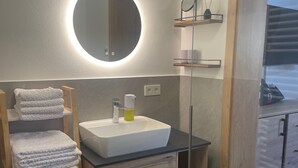A modern bathroom with a round mirror, a white sink, and a wooden towel rack. - Beagzeit Ferienwohnung (Lofer)