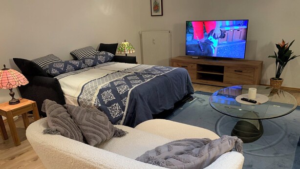 Ein gemütliches Wohnzimmer mit einer Couch, einem Glastisch, einem Fernseher und einer Lampe.