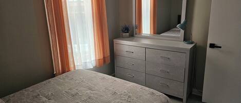 A bedroom with a bed, a dresser, a mirror, and a door.