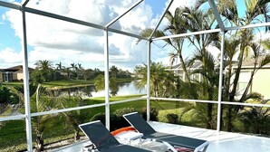 A sunroom with two lounge chairs, a view of a lake, and surrounding greenery. - Charming Lakeview Home, Heated Saltwater Pool, WiFi, All New Furniture (Venice)