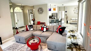 A modern living room with a sectional sofa, a red coffee table, and a dining area in the background. - Charming Lakeview Home, Heated Saltwater Pool, WiFi, All New Furniture (Venice)