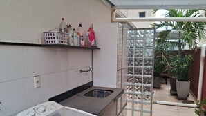 Una cocina compacta con lavadora, un lavamanos y una estantería con productos de limpieza.