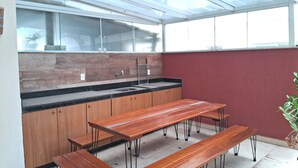 Una cocina moderna con armarios de madera, un lavamanos de acero inoxidable y una zona de comedor con bancos, protegida por vidrio.