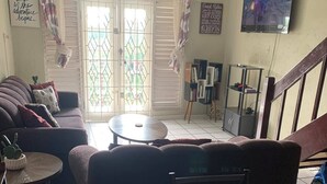 Un salon avec un canapé, une petite table ronde, un téléviseur fixé au mur et un escalier menant à l’étage.