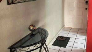 Un couloir avec un sol carrelé, une porte blanche, une petite table sur laquelle repose un globe terrestre et un mur rouge.