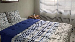 Une chambre à coucher avec un lit, une table de chevet, un miroir et une fenêtre avec des rideaux.