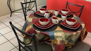 Un coin repas avec une table dressée pour six personnes, entourée de chaises, une petite table sur laquelle repose un globe terrestre, et un mur rouge orné d’un motif géométrique.
