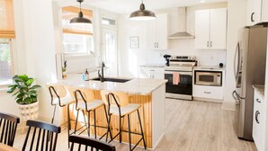 A modern kitchen with white cabinets, a central island with bar stools, stainless steel appliances, and pendant lighting. - The Lounge- Heated Private Bar, Hot Tub, Fire Pit, Sleeps 14 (Cincinnati)