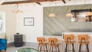 A modern interior with exposed wooden beams, a bar area with stools, and a green armchair. - The Lounge- Heated Private Bar, Hot Tub, Fire Pit, Sleeps 14 (Cincinnati)