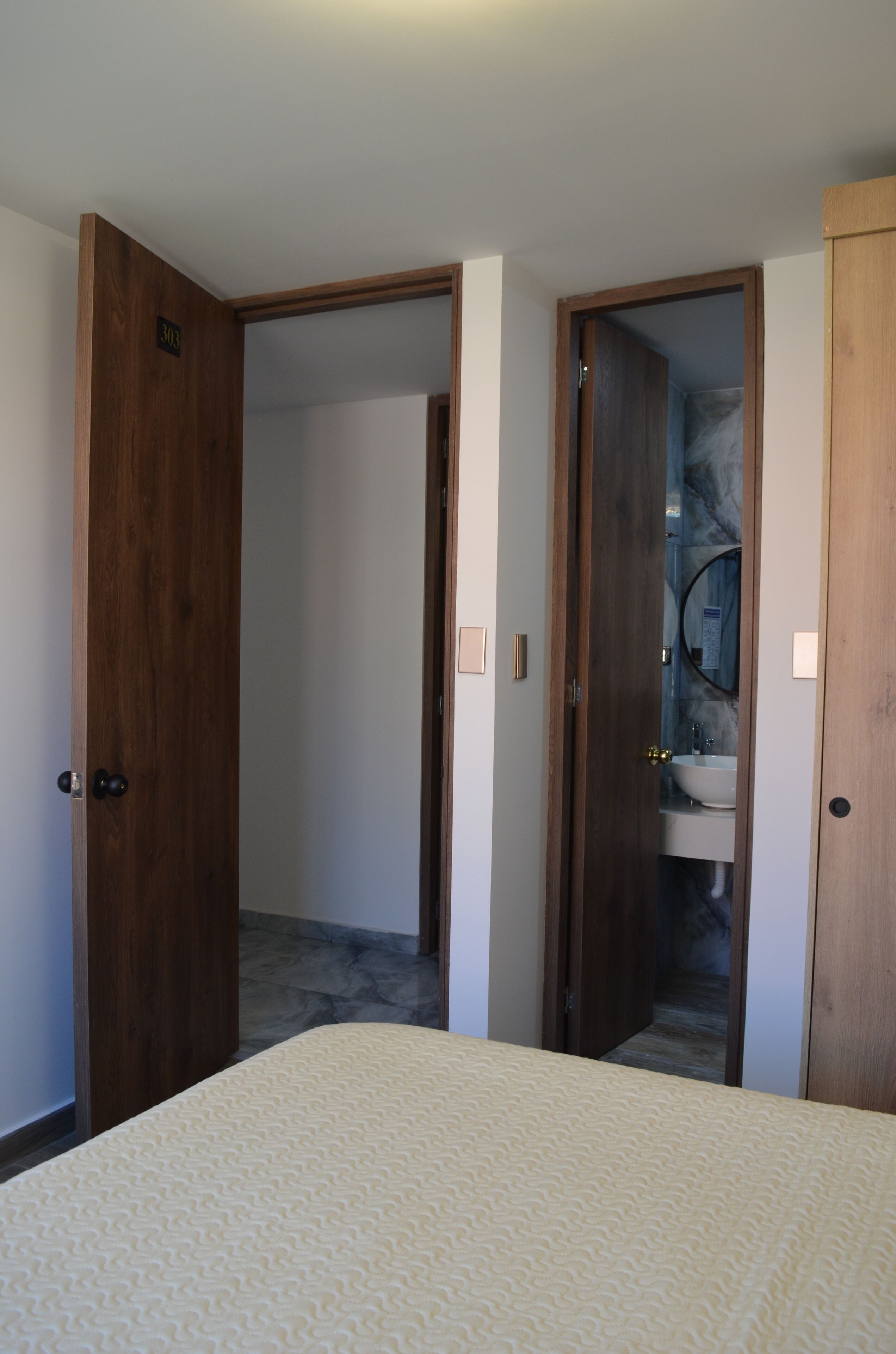 A bedroom with a bed, a wooden door, and a bathroom visible through an open door.