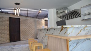 A modern interior with a marble reception desk, wooden stools, a brick wall, and a ceiling with horizontal beams.