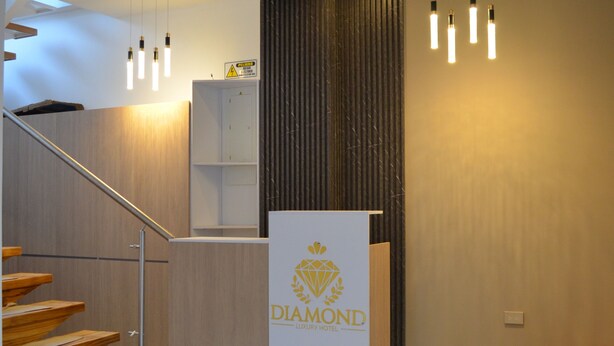 A hotel reception area with a marble floor, a wooden staircase, a reception desk with a logo, and modern lighting fixtures.
