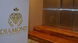 A reception desk with a sign reading "DIAMOND LUXURY HOTEL," an elevator, and a wooden bench.