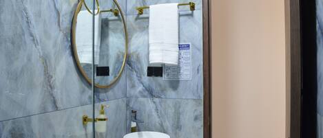 Un baño con pared de mármol, lavamanos dorado, espejo y toallero.