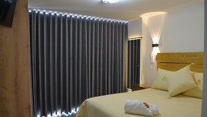 A hotel room with a large bed, a wooden headboard, and a curtain with a lighted bottom edge.