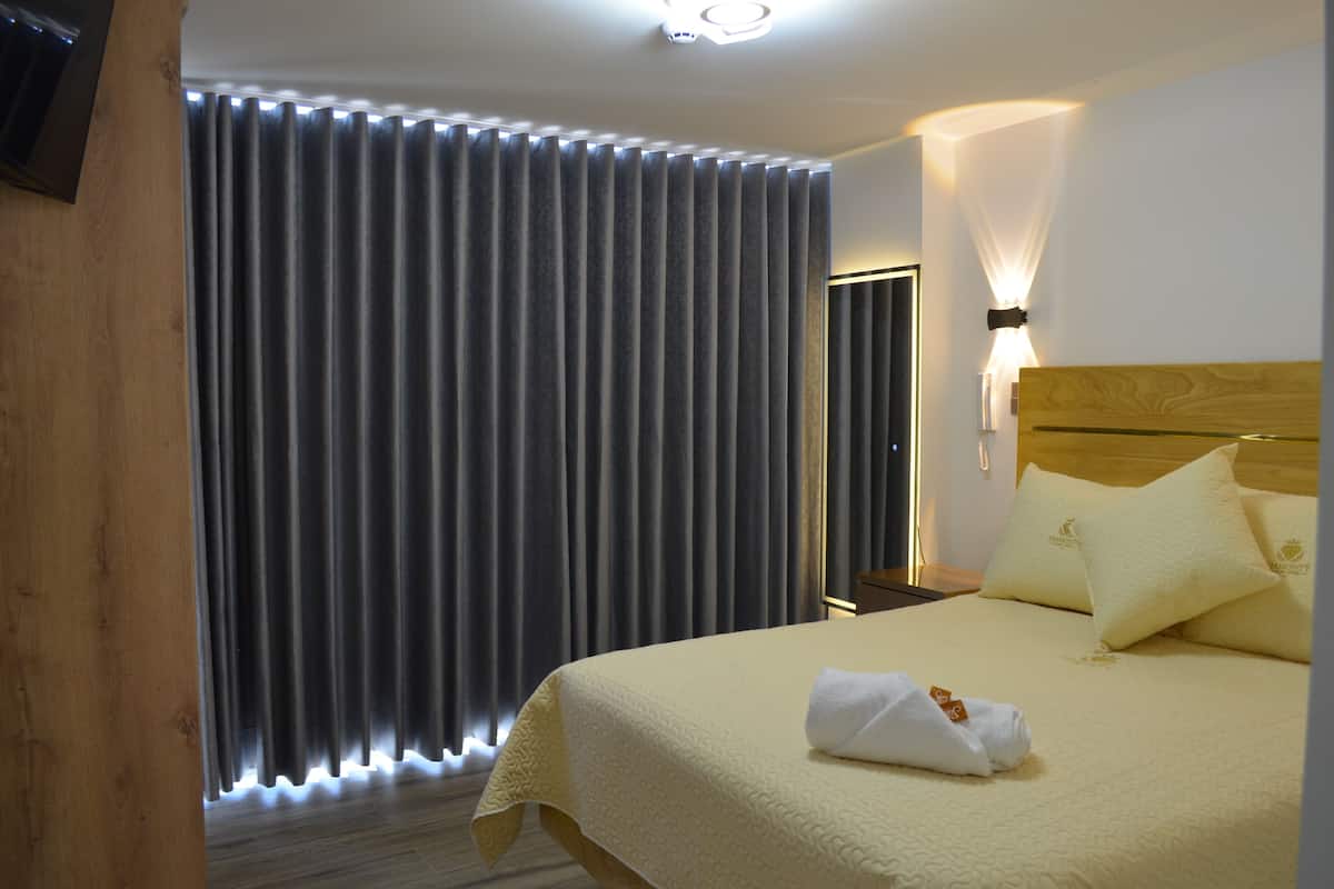 Une chambre d’hôtel avec un grand lit, une tête de lit en bois et un rideau dont le bord inférieur est illuminé.