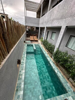 Una piscina con bordes de azulejos, rodeada por un muro de hormigón y una valla de madera.