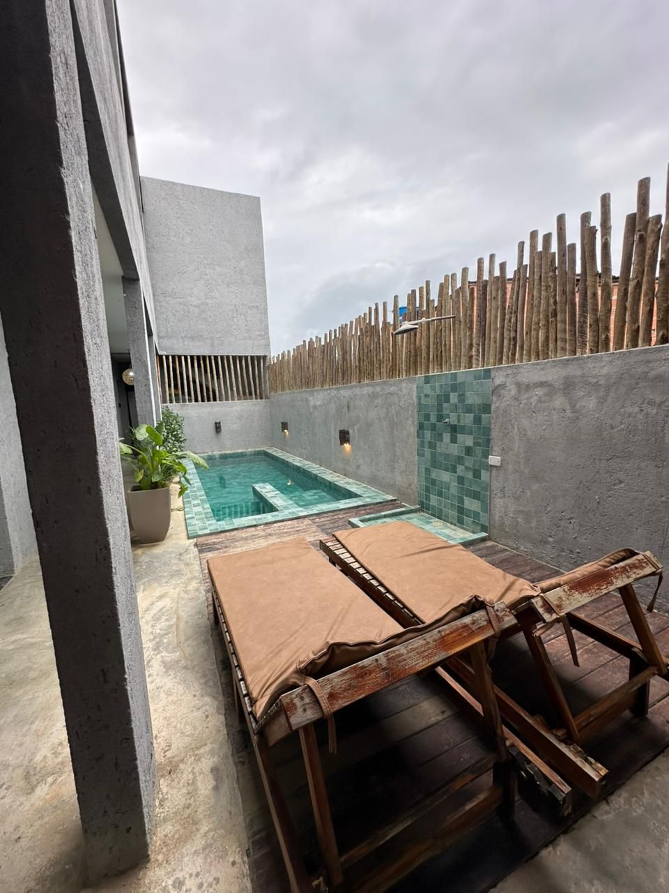 A small outdoor pool area with a wooden fence, a seating area with cushions, and a potted plant.