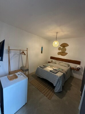 Ein Schlafzimmer mit einem Bett, Nachttischen, einer Pendelleuchte, einem Wandventilator und einem kleinen Schreibtisch mit einem Korb.