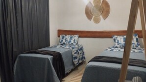 Ένα υπνοδωμάτιο με δύο κρεβάτια, ένα ξύλινο προσκέφαλο και ένα διακοσμητικό κρεμασμένο στον τοίχο, φτιαγμένο από υφαντό υλικό.