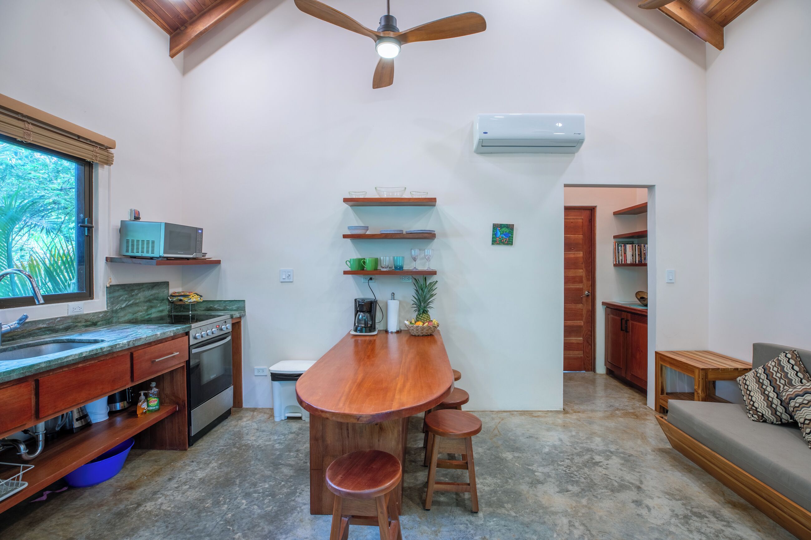 Una cucina con bancone in legno, sgabelli, ventilatore a soffitto e condizionatore.
